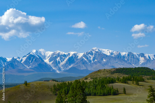Landscape of snow-capped mountains  with green hilly valley a fresh summer day under a blue sky with white clouds and sun rays in Altai mountains