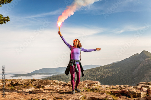 A woman in the wild mountains gives a distress signal SOS using Falsch feuer torch from which comes a bright flame and orange smoke, Concept of emergency situation during hike in the woods photo