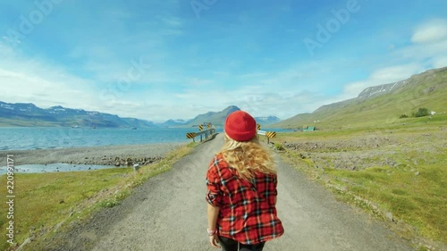 Slow motion epic colorful shot of young blond woman in red beanie hipster hat and millennial checkered shirt walk on empty road in amazing travel destrination, travel inspiration for wanderlust photo