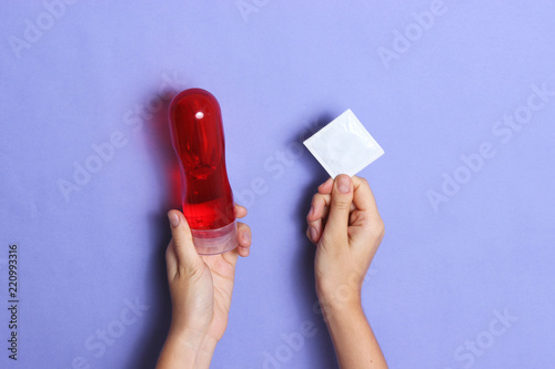 Photography Intimate lubrication and condom in hands on a colored background