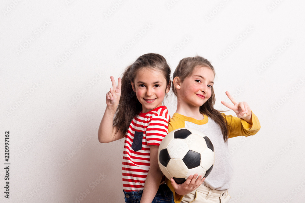 Small girls with a soccer ball standing in a studio, showing victory sign. Small girls with a soccer ball standing in a studio, showing victory sign.