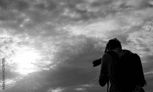 Young unidentifiable teenage boy taking outdoor pictures at sunset in black and white.