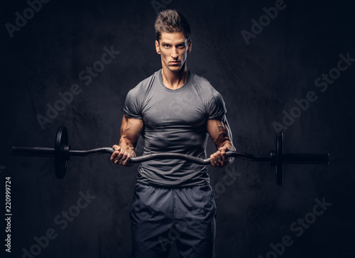 Handsome sportsman with stylish hair dressed in a sportswear doing the exercises with the barbell.