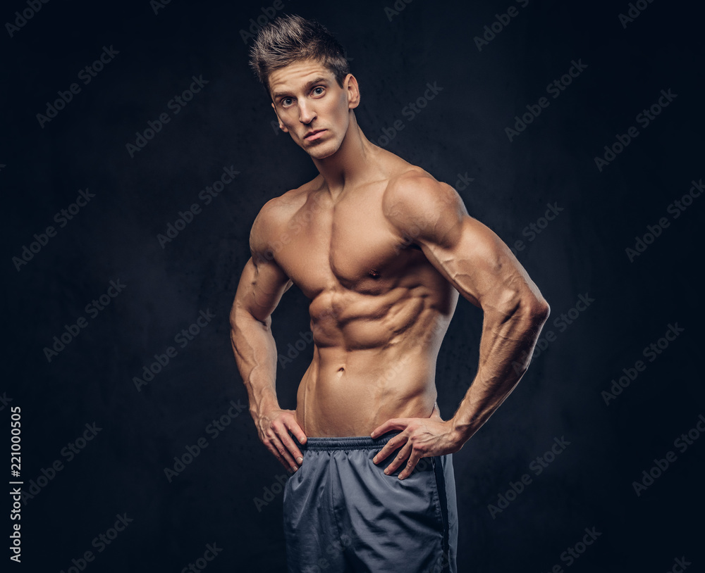 Handsome shirtless ectomorph bodybuilder with stylish hair posing on a dark background.