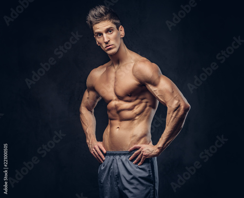 Handsome shirtless ectomorph bodybuilder with stylish hair posing on a dark background.