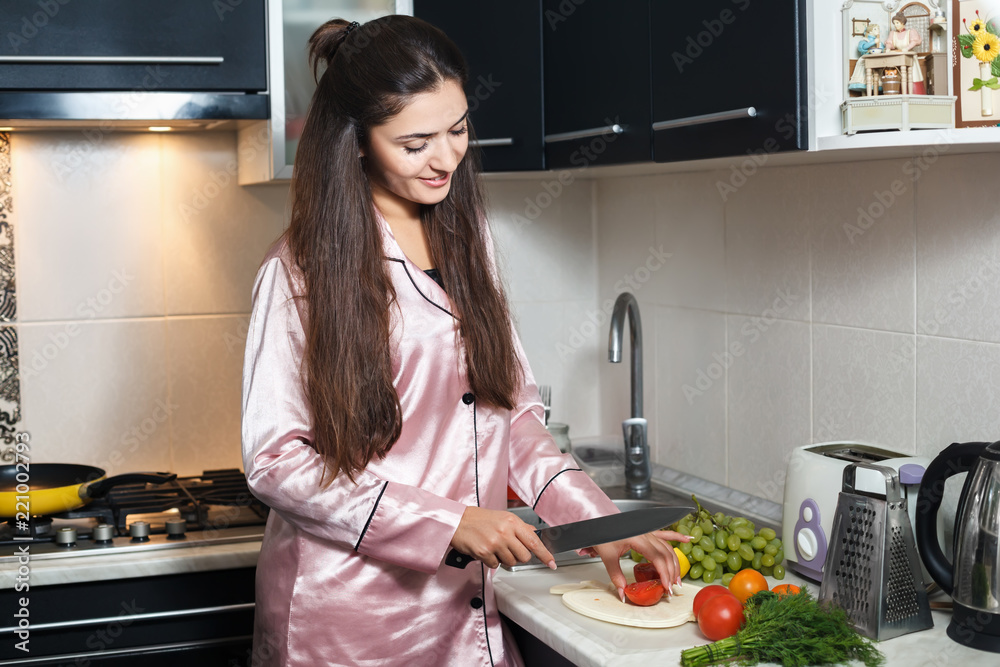 A young smiling woman is making a salad in the kitchen. Healthy lifestyle