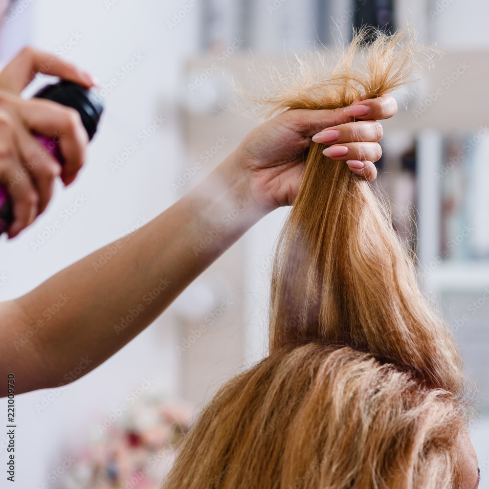 Fototapeta premium Closeup of hairdresser making modern hairstyle using spray