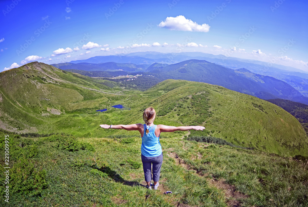 Young woman  on a stone   with raised hands on the  top of   mount .Green fir trees and blue lake against the background of the Carpathian mountains in summer, top view ,Carpathian ,Dragobrat,Ukraine