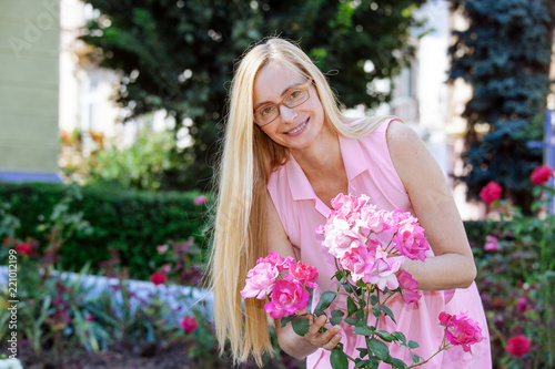 real portrait woman happy blonde middle age nature summer long hair sunlight fifty plus 50 pink roses flowers glasses