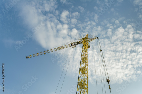 yellow tower crane on a background of blue sky with clouds, industry abstract background
