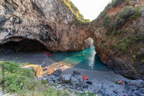 Fototapeta Naklejka Na Ścianę i Meble -  bathers in Arcomagno with a ray of sun at sunset (Arco magno), natural arch in San Nicola Arcella, Calabria, Italy