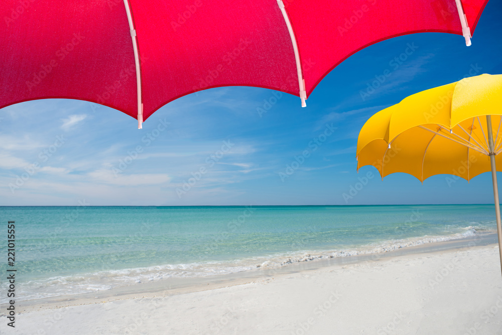 View of perfect untouched pristine white sand blue water beach with wispy cirrus clouds from under large red umbrella