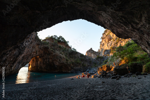 bathers in Arcomagno with a ray of sun at sunset (Arco magno), natural arch in San Nicola Arcella, Calabria, Italy