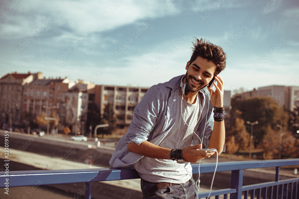 Fototapeta premium Young man listens to music via smartphone in the city