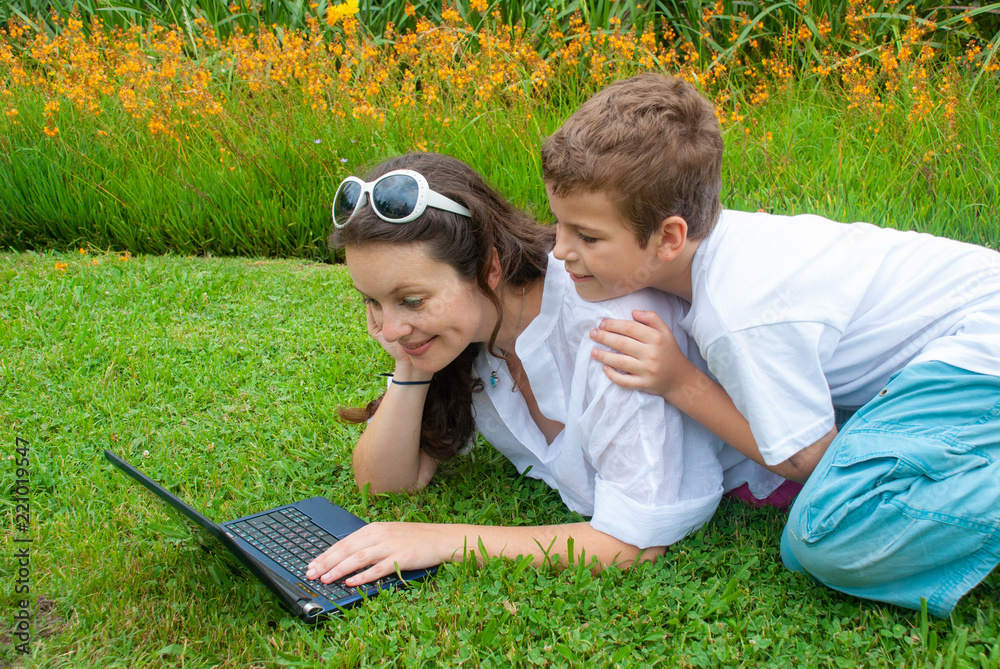 mother with her son on the grass in the park with computer