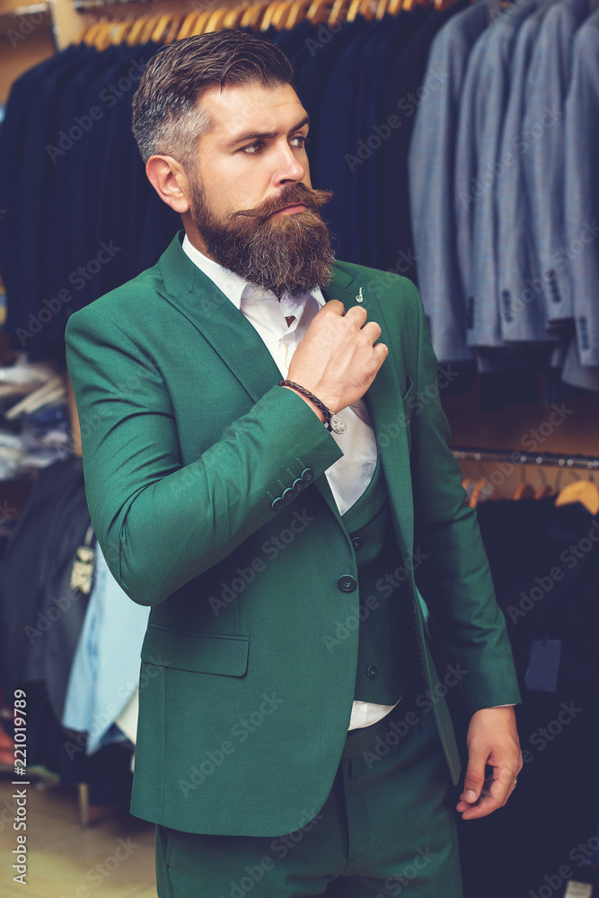 Men suits in a showcase of a clothing shop. Bearded caucasian man wearing  green suit. Handsome