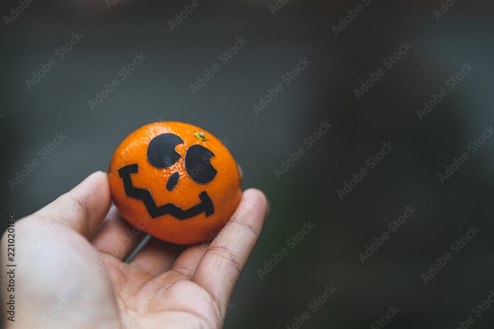 an oranges pumpkin face painting with scary on halloween party day on hand with blur background. an oranges pumpkin face painting with scary on halloween party day on hand with blur background.
