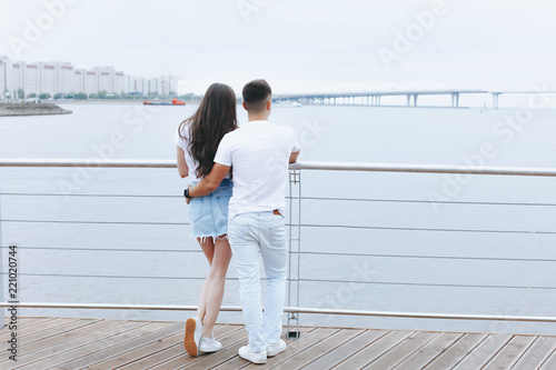 Young loving couple stands with their backs on sea promenade