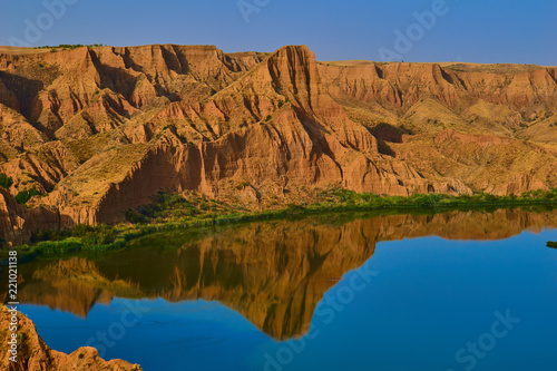 Beautiful landscape with red rocks and lake in the foreground with reflection in the water of the mountains with clear sky in the Barrancas de Burujon, Toledo, Spain photo