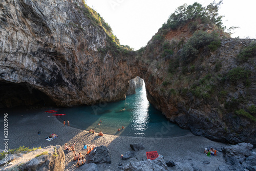 Fototapeta Naklejka Na Ścianę i Meble -  bathers in Arcomagno with a ray of sun at sunset (Arco magno), natural arch in San Nicola Arcella, Calabria, Italy