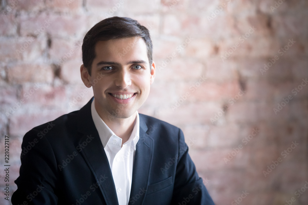 Head shot of portrait of smiling and happy successful male businessman or business owner wearing suit sitting in office at workplace. Looking at camera Head shot of portrait of smiling and happy successful male businessman or business owner wearing suit sitting in office at workplace. Looking at camera