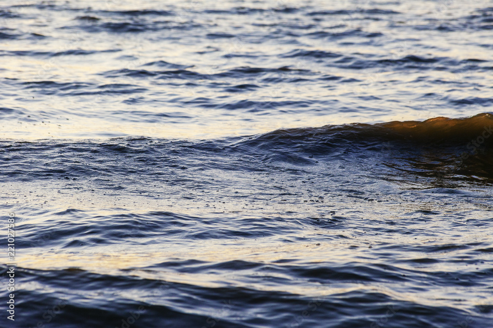Waves on the sandy shore of a large river. The rays of light are reflected in the waves. Waves on the sandy shore of a large river. The rays of light are reflected in the waves.