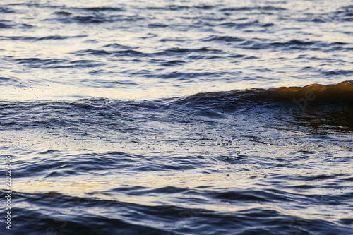 Waves on the sandy shore of a large river. The rays of light are reflected in the waves.
