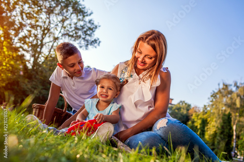 Happy family spending time outdoors sittting on grass in park. Mom with two children smiling. Family values