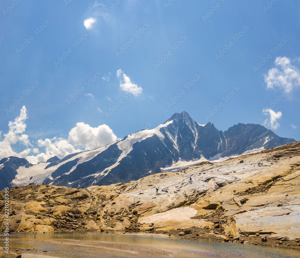 Smoothed out and round stone formation with two hikers in front of the Grossglockner Mountain in Austria Smoothed out and round stone formation with two hikers in front of the Grossglockner Mountain in Austria