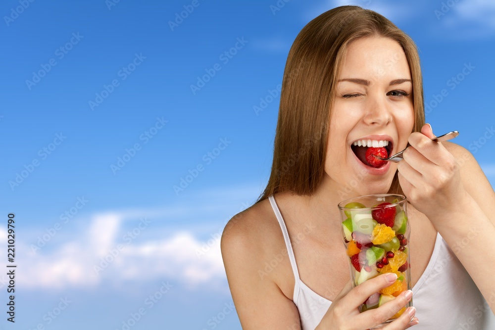 Young woman eating fruits from glass on blurred background Young woman eating fruits from glass on blurred background