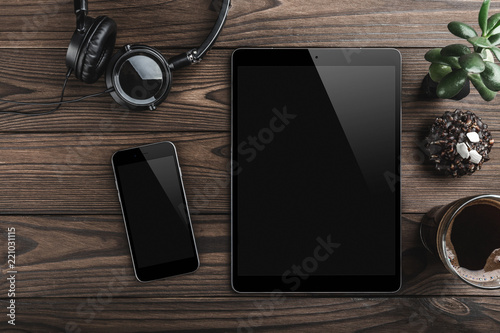 Mock-up blank screen tablet and smartphone, office desk table with headphones, biscuits and coffee cup. Top view
