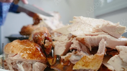 Man carving roasted turkey for Thanksgiving holiday meal. The roasted poultry is traditionally served at the autumn feast. Shallow depth of field of the platter of sliced white meat and rustic kitchen