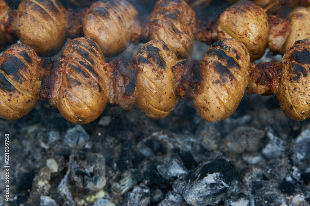 Baby potatoes grilled on skewers with lamb fat meat over coals