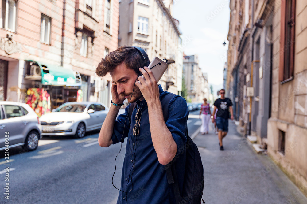 oung handsome man listening music via headphones while standing on the street