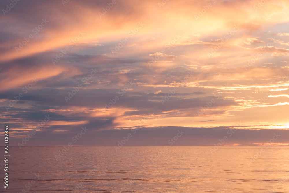 Sunset seascape, orange, blue, yellow, magenta, gold sky reflected in the sea pacific ocean, background photo of sun setting over horizon amid beautiful clouds