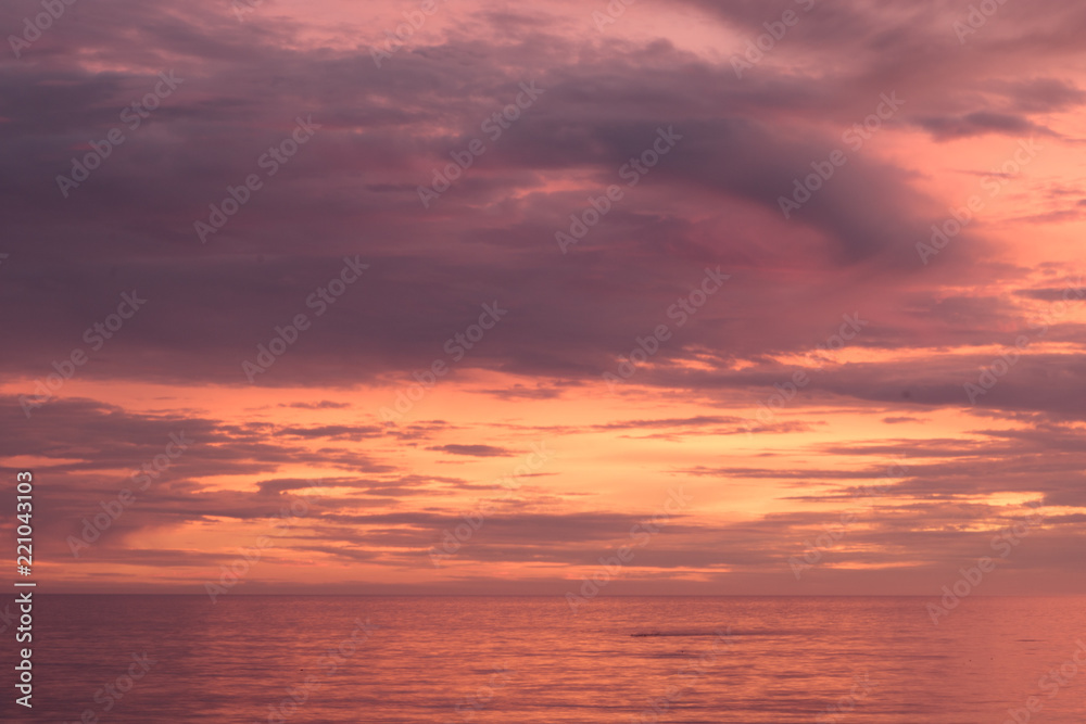 Sunset seascape, orange, blue, yellow, magenta, gold sky reflected in the sea pacific ocean, background photo of sun setting over horizon amid beautiful clouds