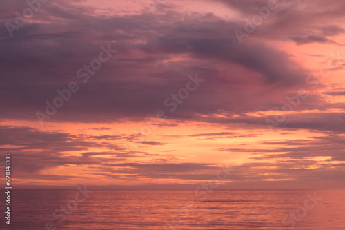 Sunset seascape, orange, blue, yellow, magenta, gold sky reflected in the sea pacific ocean, background photo of sun setting over horizon amid beautiful clouds © Mary