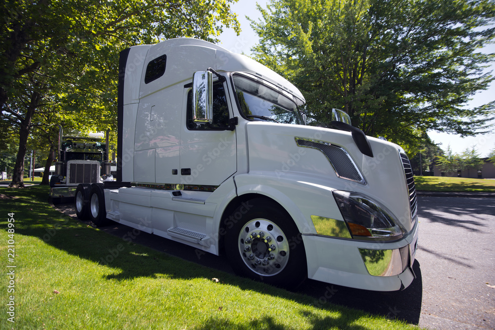 Big rig semi truck tractors parking on the road with green grass and shady trees