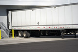 Long semi trailer loading industrial cargo in warehouse dock with gates