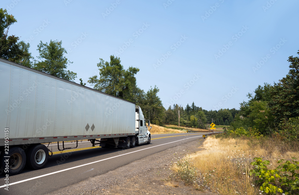 White big rig semi truck transporting cargo in dry van semi trailer on winding green road