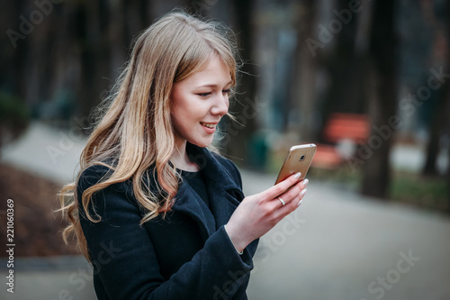 Outdoor portrait of a romantic, pretty elegant business long-haired woman, enjoying a stroll through the city with a phone in hand. The picture of a charming girl in a hat with curly hair makes hersel