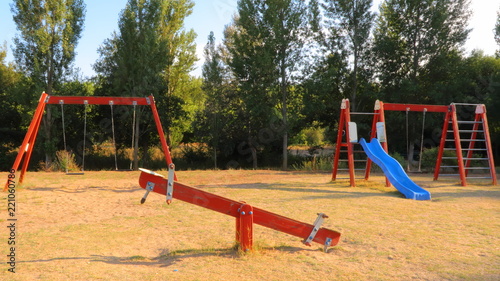 Paisaje con parque para niños con columpios de madera de color rojo y fondo de arboles y cielo azul al atardecer