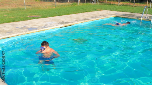 Niños nadando en piscina en verano de vacaciones al atardecer con los rayos de sol