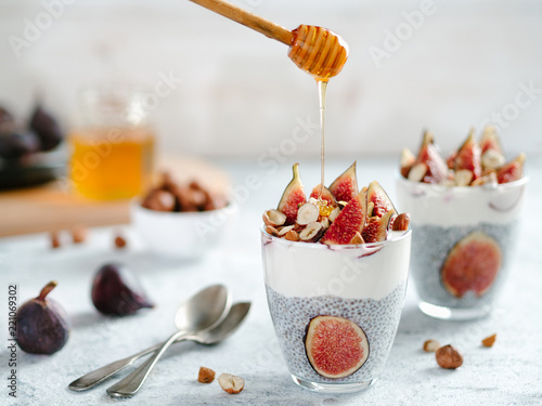 Healthy chia pudding with yogurt, figs and nuts in glass. Ideas and recipes for healthy breakfast, snack or dessert. Honey drips into glass with chia seeds pudding. Copy space for text.