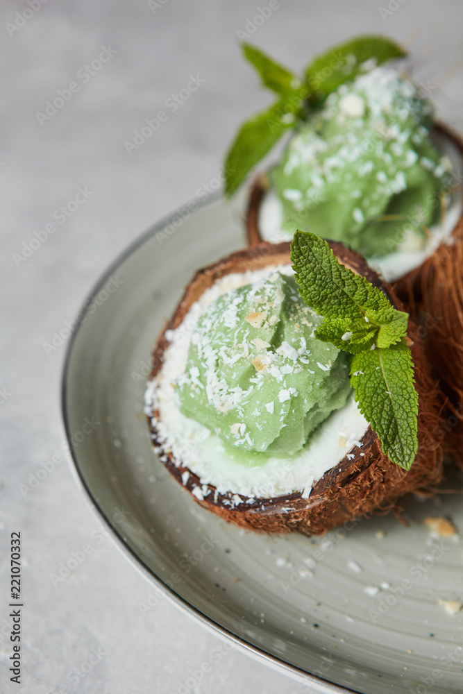 Close-up of delicious green ice cream with mint leaf in a coconut shell on a gray plate.