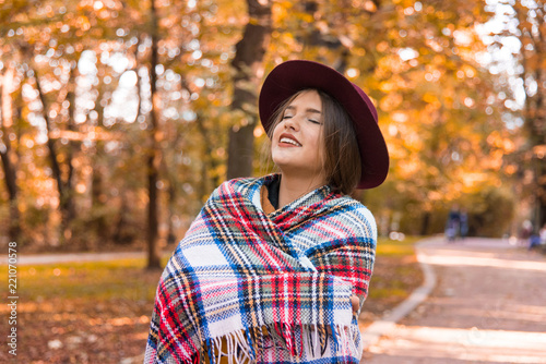 Beautiful young woman in a stylish vintage scarf walks in the park in autumn day. The teenage girl, autumn portrait. Beautiful girl in red floppy hat and shawl. Retouched, vibrant color, copy space.