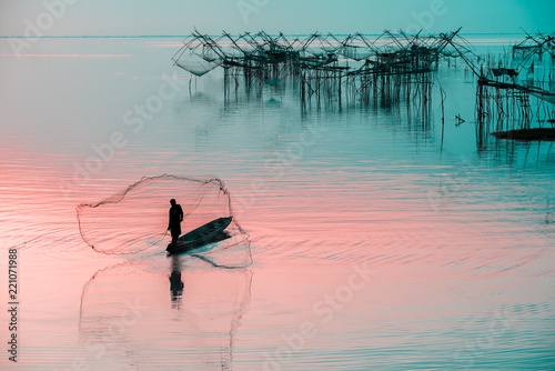 Fototapet Silhouette of fishermen using coop-like trap catching fish in lake with beautiful scenery of nature morning sunrise