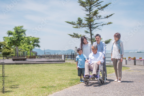 公園で微笑む車椅子のシニア男性と三世代家族