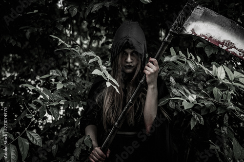 Asian woman dress black as Grim Reaper of death and holding or wielding a large scythe in Halloween festival. Halloween concept.