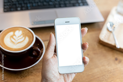 hand woman using a telephone, empty screen smart phone and computer on wooden table In the coffee shop. with clipping path